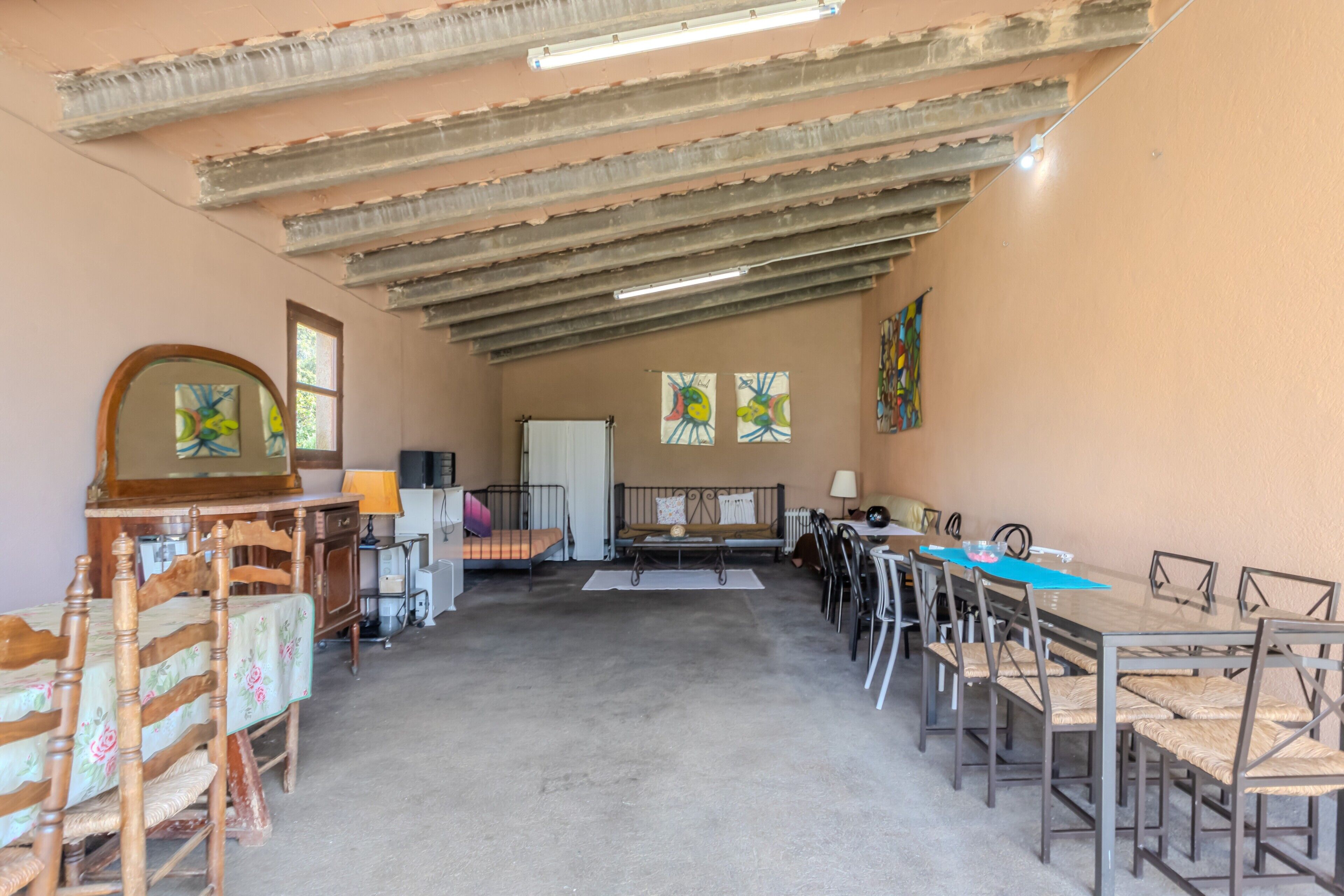 A room with a long table, chairs, a sofa, a mirror, and artwork on the walls.
