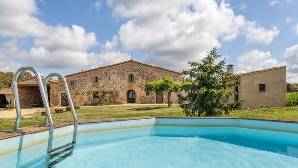 A swimming pool with metal ladders, a stone building with a tiled roof, and a clear sky.