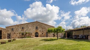 A stone building with a tiled roof, a covered patio with outdoor seating, and a grassy courtyard.