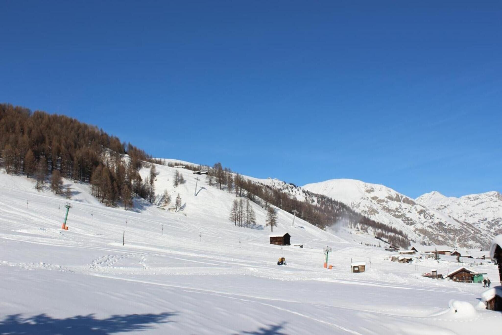 Pista de esqui coberta por neve, com edifícios e árvores ao fundo.