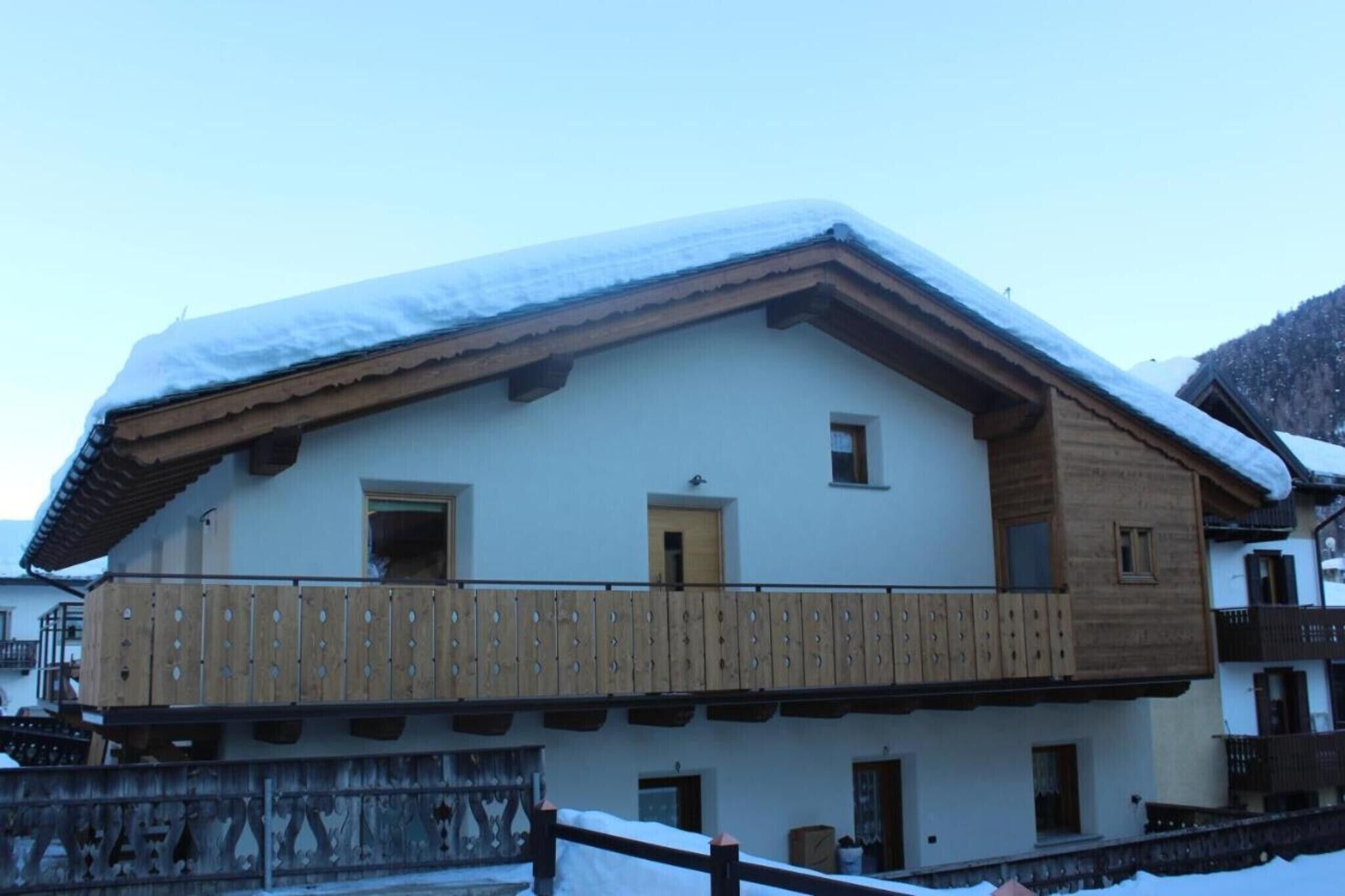 A two-story building with a balcony, wooden railings, and snow on the roof.