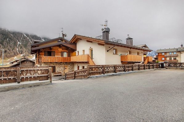 A chalet-style building with wooden balconies, a stone facade, and a mountain backdrop.
