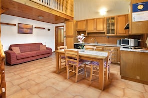A cozy kitchen with wooden cabinets, a dining table with chairs, a red sofa, and a view of the outside.