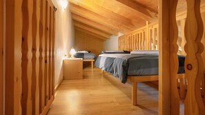 Ein Holzinnenraum mit schrägverdeckter Decke, einem schmalen Gang und zwei Betten mit Holzgestellen.