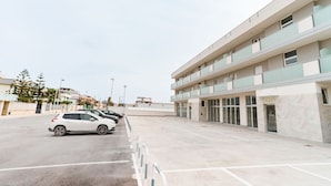 A modern building with a parking lot, multiple floors, and a row of parked cars.