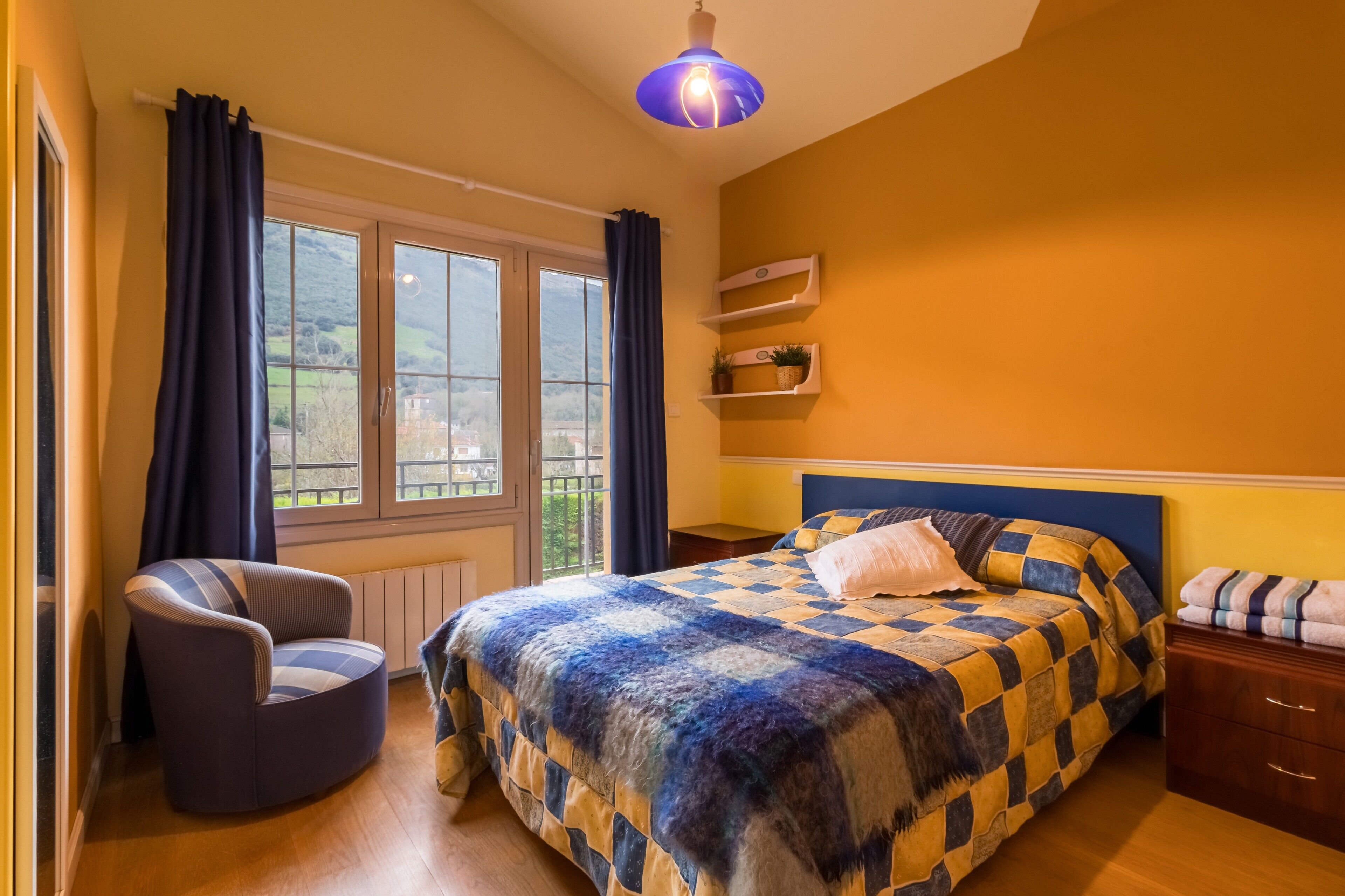 A bedroom with a bed, a chair, a nightstand, a shelf with plants, and a window with curtains.