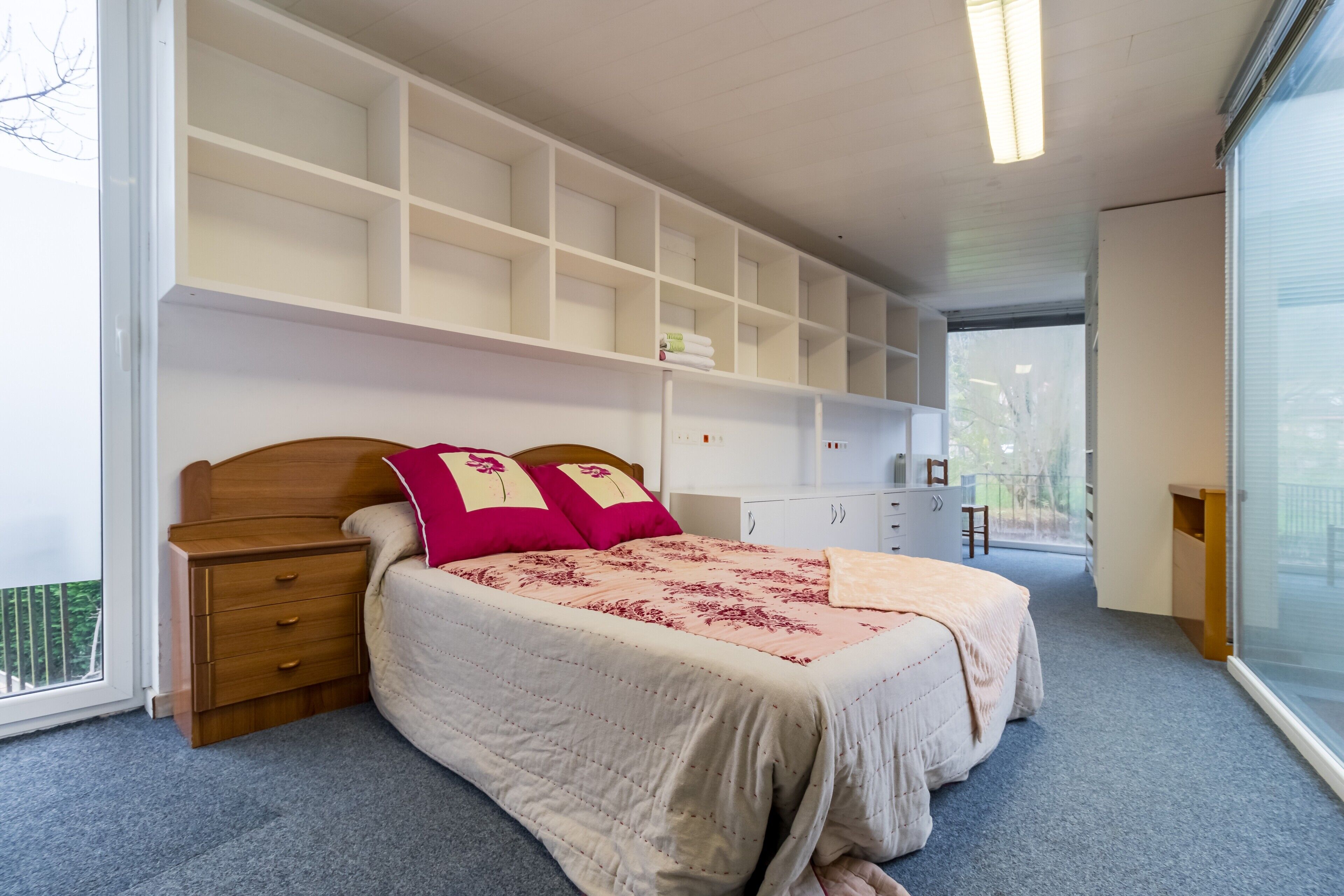 Een slaapkamer met een bed, nachtkastje, dressoir en inbouwplanken.