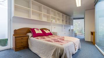 Een slaapkamer met een bed, nachtkastje, dressoir en inbouwplanken.