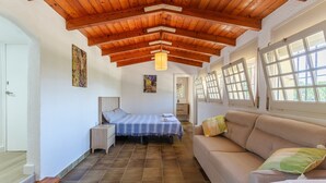 A bedroom with a wooden ceiling, a bed, a nightstand, a sofa, and a window with a view.