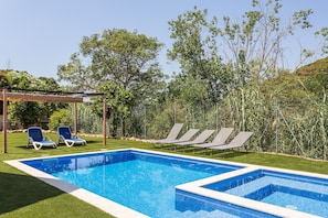 Une piscine rectangulaire aux carreaux bleus, entourée de gazon synthétique vert, et agrémentée de deux chaises longues.