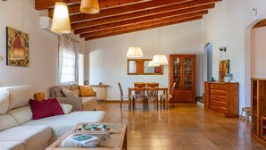 A spacious living room with a high wooden ceiling, a dining area with chairs and a table, and a kitchen area with cabinets and a refrigerator.