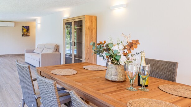 A dining area with a wooden table, woven chairs, a vase with flowers, and a bottle of champagne.