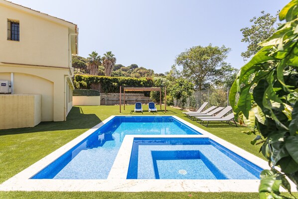 A rectangular swimming pool with two lounge chairs and a pergola in a backyard.