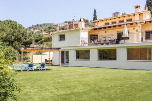 A two-story house with a swimming pool, a covered patio, and a view of a hilly area.