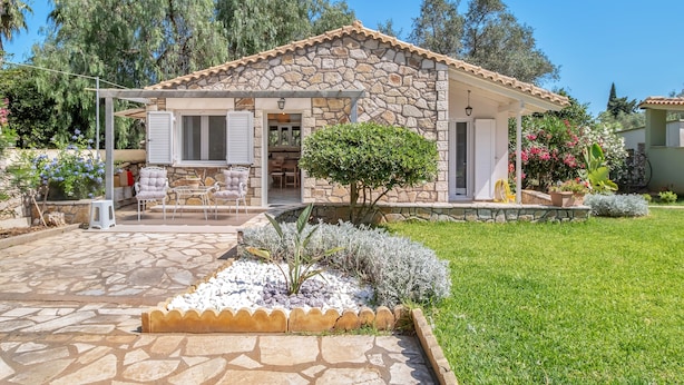 Une maison en pierre avec un toit en tuiles, une terrasse avec des meubles d’extérieur et un jardin bien entretenu.