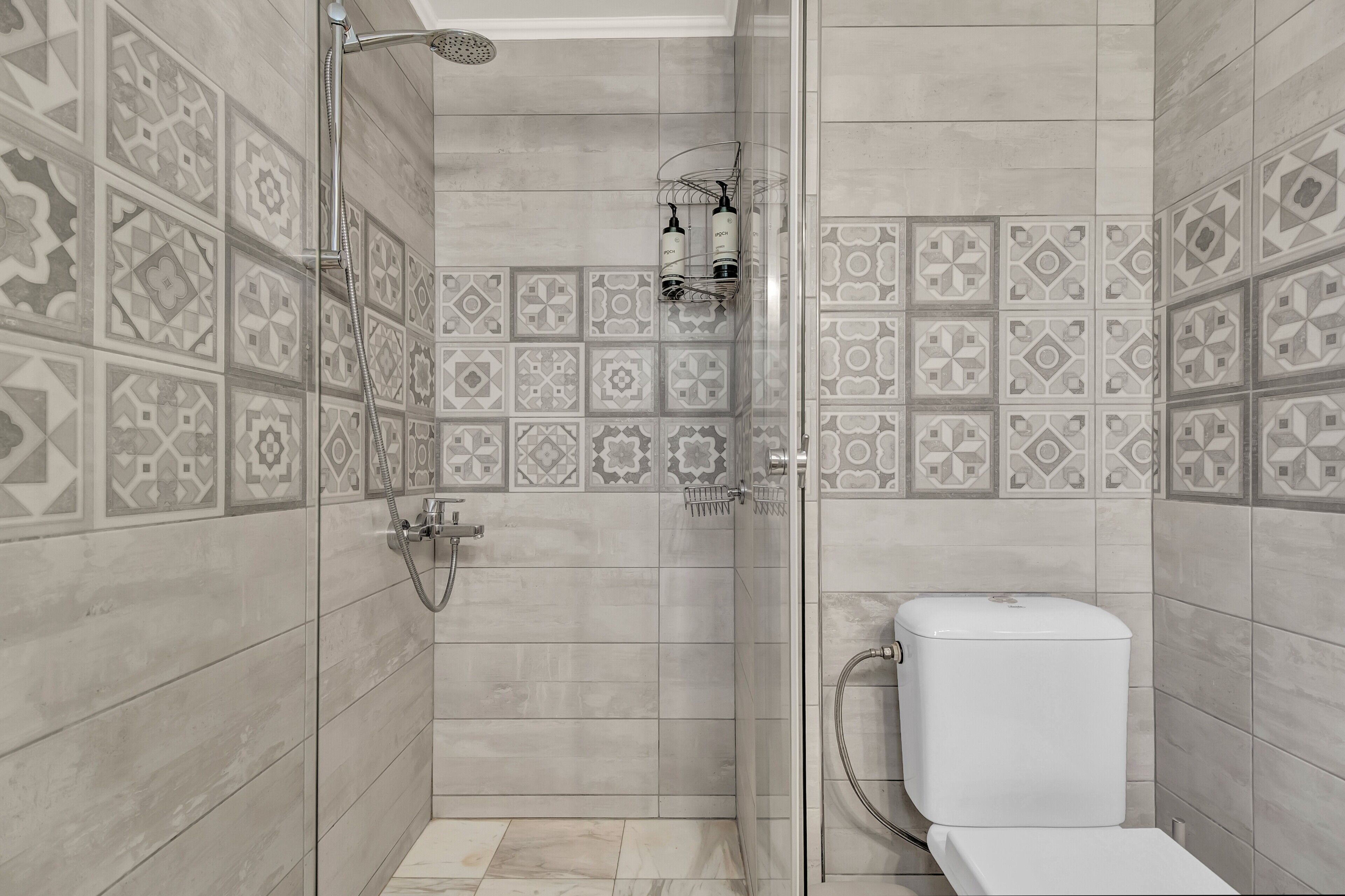 Ducha con puerta de vidrio, inodoro y azulejos decorativos en las paredes.