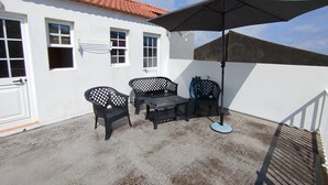 A patio with a table and chairs, a covered umbrella, and a white building with a red-tiled roof. - Apartment 'Moradia Machado' with Private Terrace, Balcony and Wi-Fi (Topo Calheta São Jorge Açores)