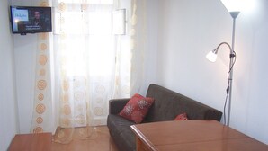 A living room with a sofa, a small table, a TV mounted on the wall, and a floor lamp. - Apartment 'Moradia Machado' with Private Terrace, Balcony and Wi-Fi (Topo Calheta São Jorge Açores)