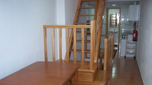A wooden dining table with chairs, a staircase with a wooden railing, and a kitchen area with cabinets and a fire extinguisher. - Apartment 'Moradia Machado' with Private Terrace, Balcony and Wi-Fi (Topo Calheta São Jorge Açores)