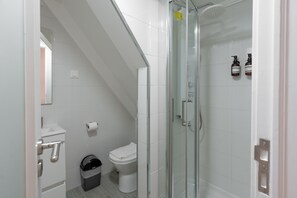 Un baño con inodoro, un cubo de basura y zona de ducha con mampara de vidrio.