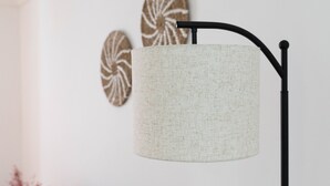 Une pièce avec un canapé beige, une petite table ronde, un lampadaire et deux éléments de décoration murale.