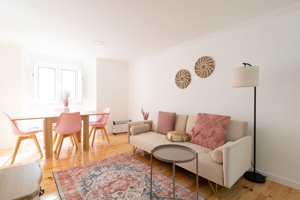 Una sala de estar moderna con un sofá color beige, sillas rosadas, una mesa redonda de centro y una alfombra estampada.