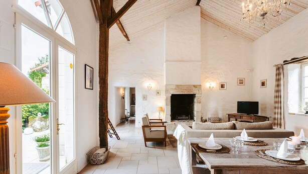 Een ruime woonkamer met een open haard, een eettafel gedekt voor vier personen en een bank.