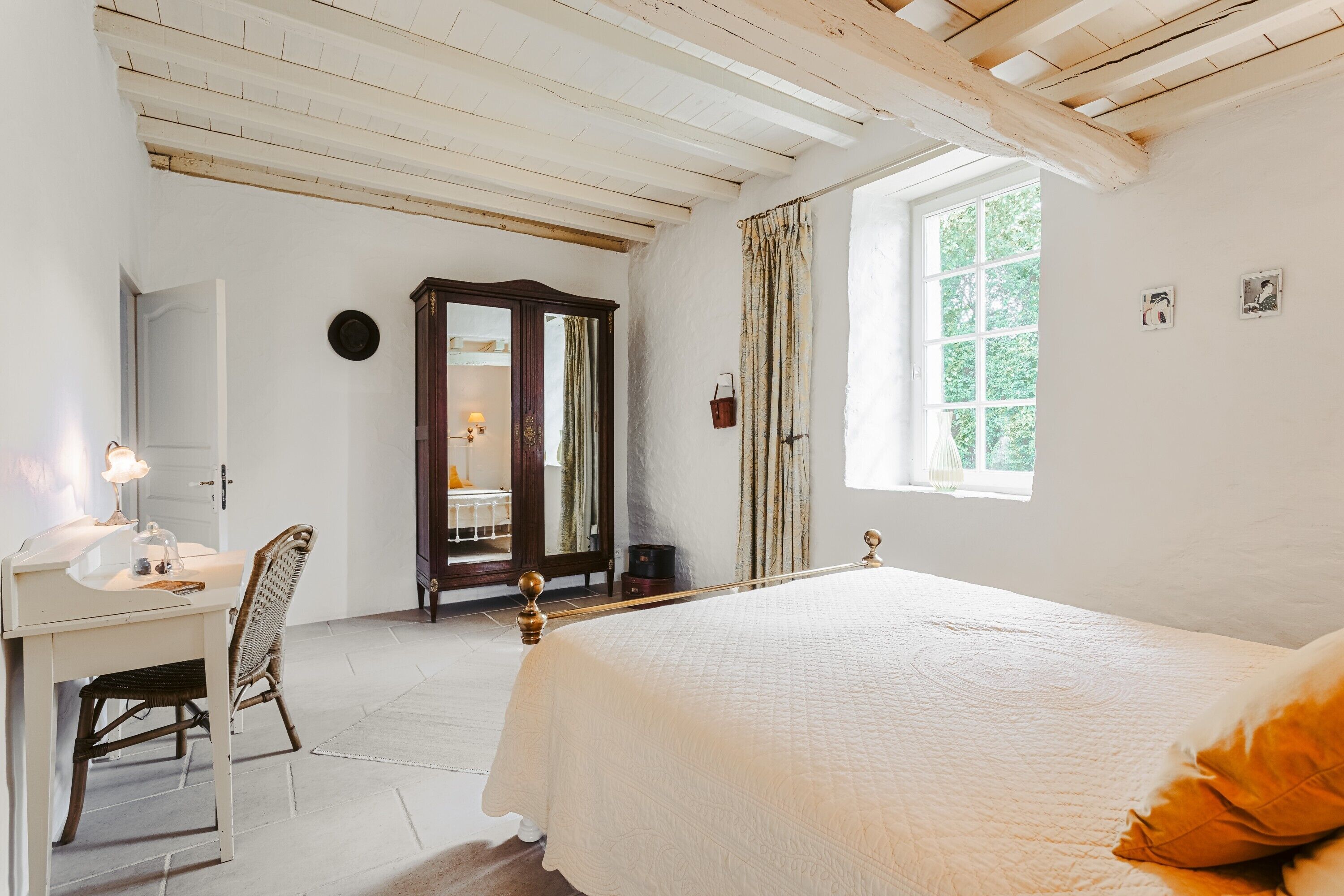 Ein Schlafzimmer mit Bett, Schreibtisch, Stuhl, Spiegel, Fenster und Tür.