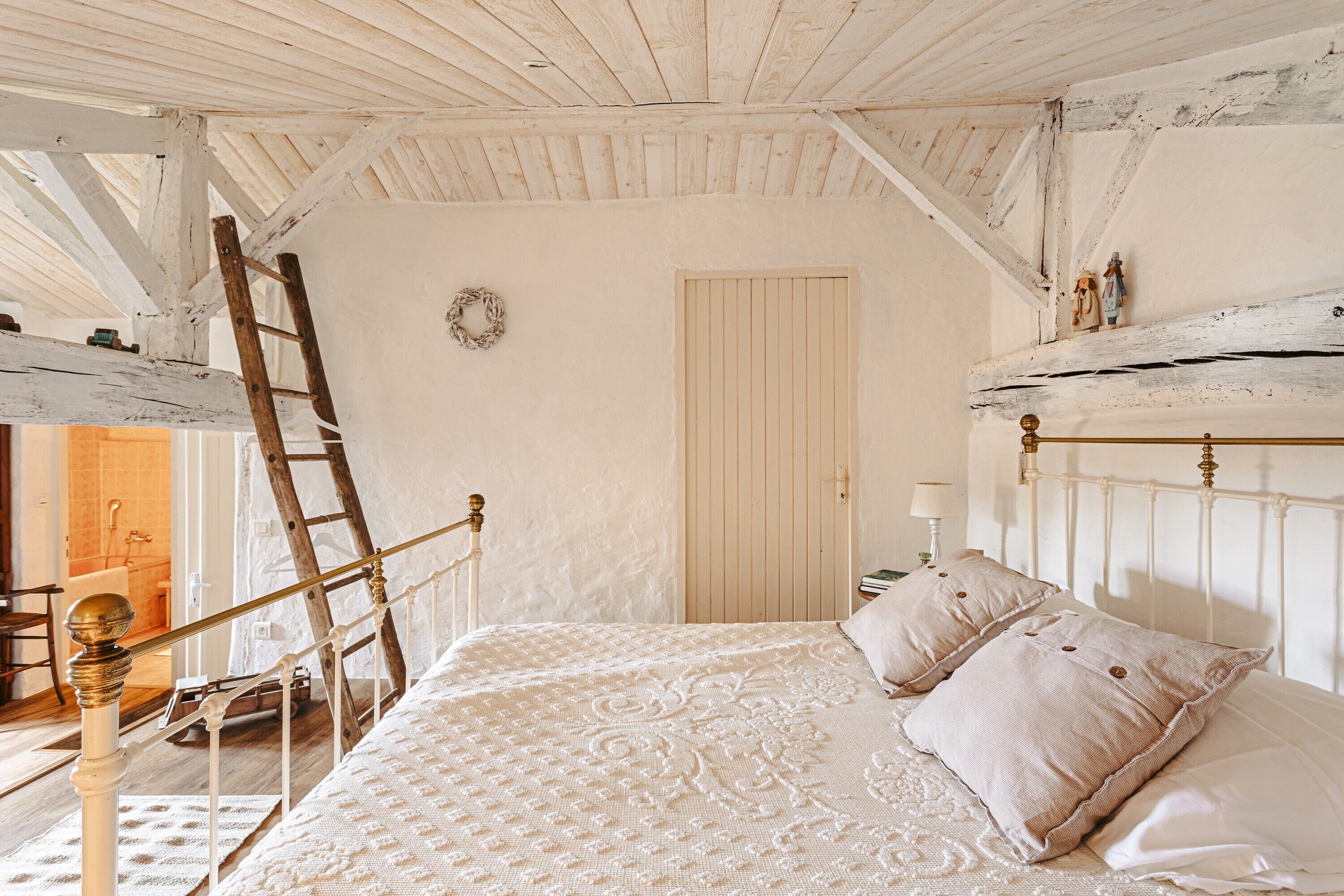 A bedroom with a wooden ladder, a bed with patterned bedding, a white door, and a small shelf with decorative items.