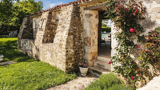 Un vieux bâtiment en pierre, avec un toit recouvert de tuiles, une petite entrée et un pot de fleurs.