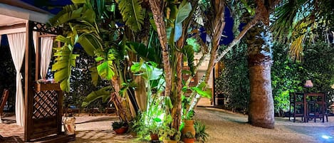 A tropical garden with a gazebo, potted plants, and a palm tree.