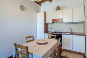A compact kitchen with white cabinets, a stove, and a sink. There is a dining table with chairs and a bowl on it.