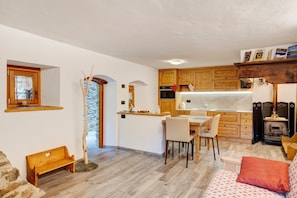 A cozy kitchen with wooden cabinets, a dining area with chairs, a bench, and a sofa with a red pillow.