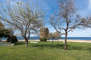 A grassy area with a stone tower and trees, a clear sky, and a body of water in the background.