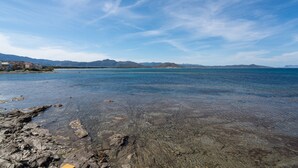 Un paisaje costero con aguas transparentes, costa rocosa y montañas a lo lejos.