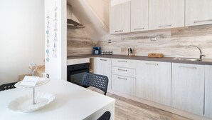Una cocina moderna con armarios de madera clara, un lavamanos de acero inoxidable y una zona de comedor con una mesa blanca y una silla negra.
