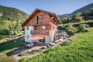 Een houten chalet met een balkon, een rode parasol en uitzicht op een bergachtig landschap.