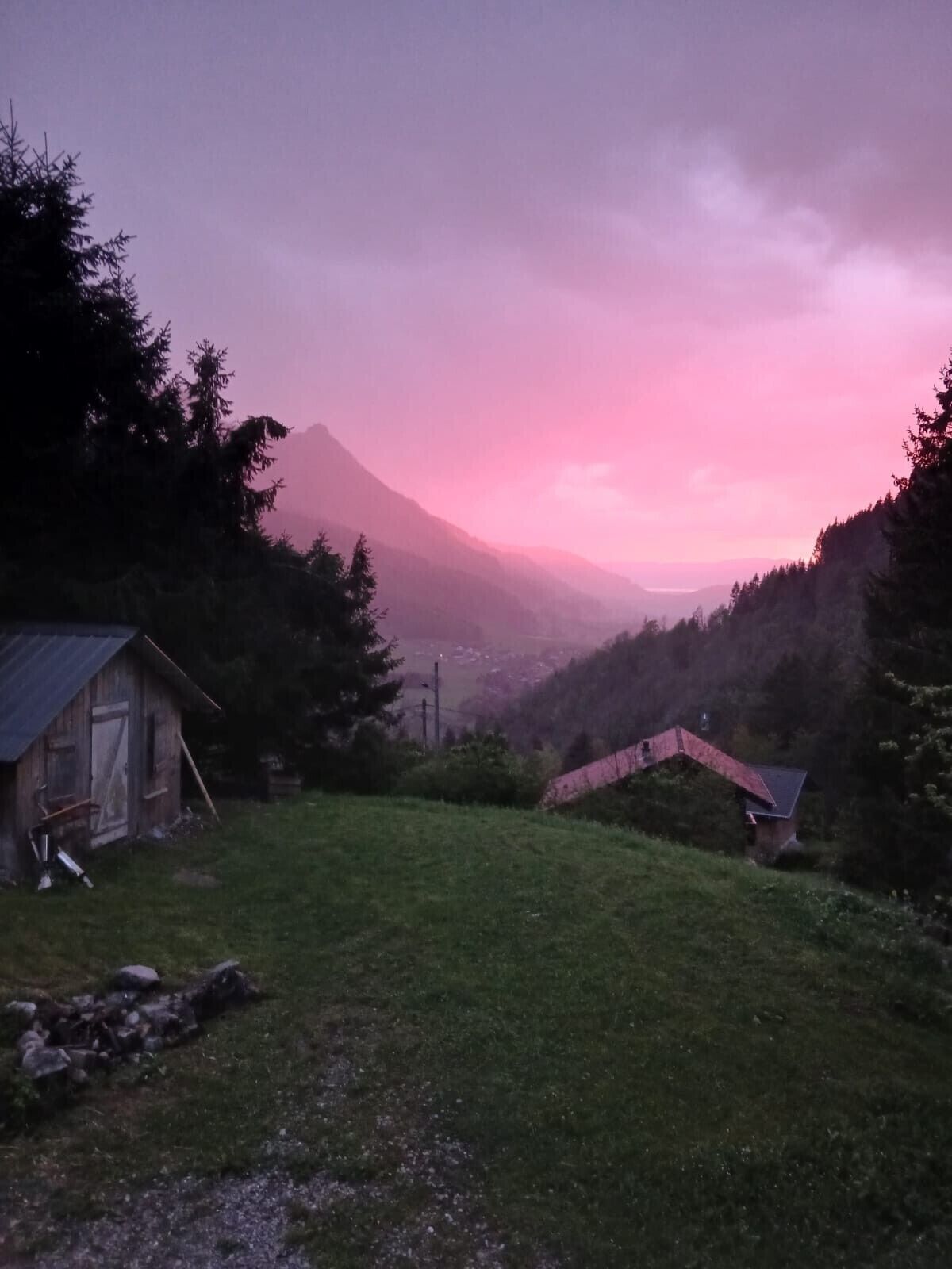 Un paisaje rural con una montaña, una pequeña cabaña de madera y una estructura de techo rojo.
