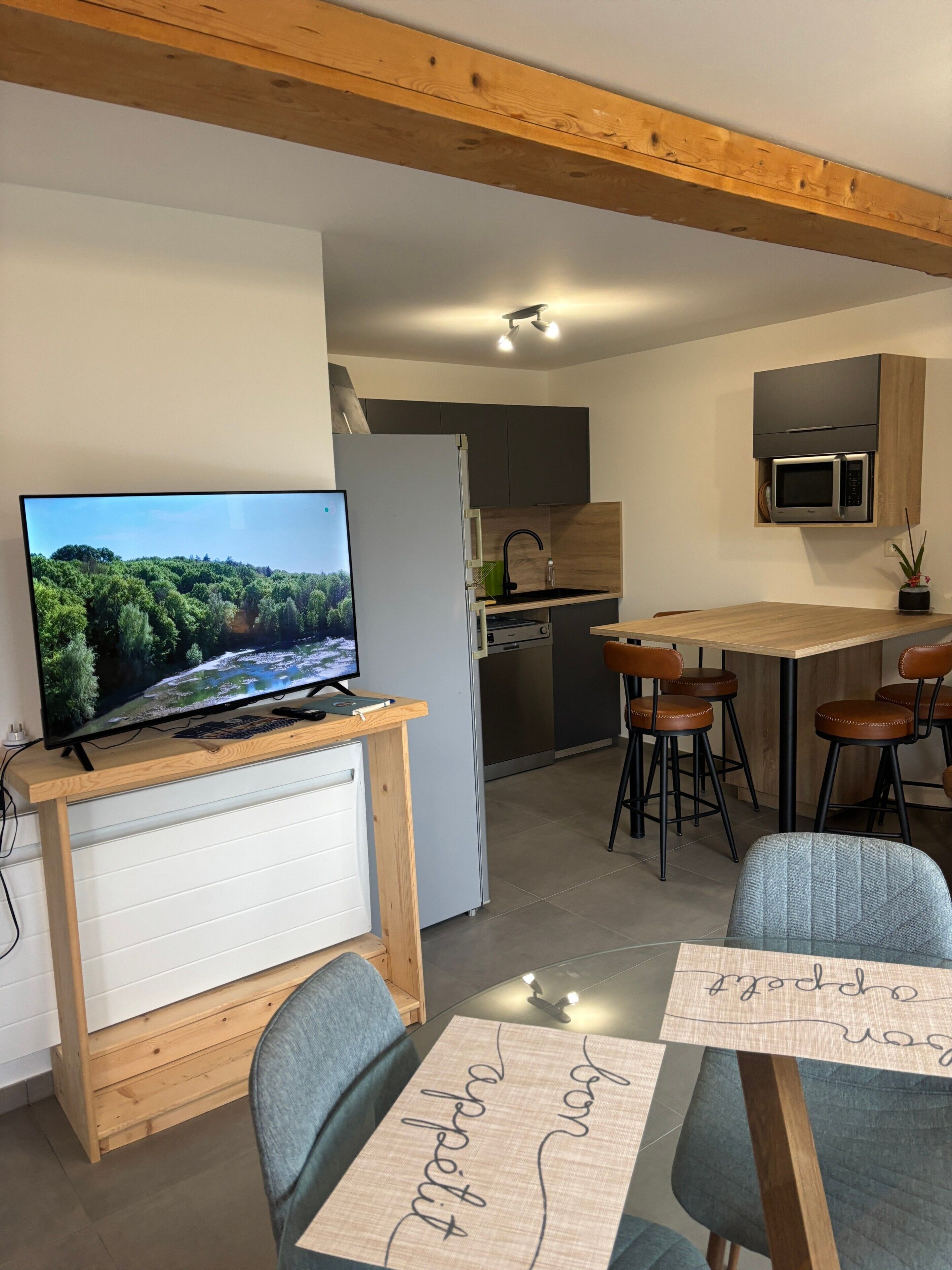 A modern kitchen with a built-in microwave, a TV on a wooden stand, and a dining area with bar stools.