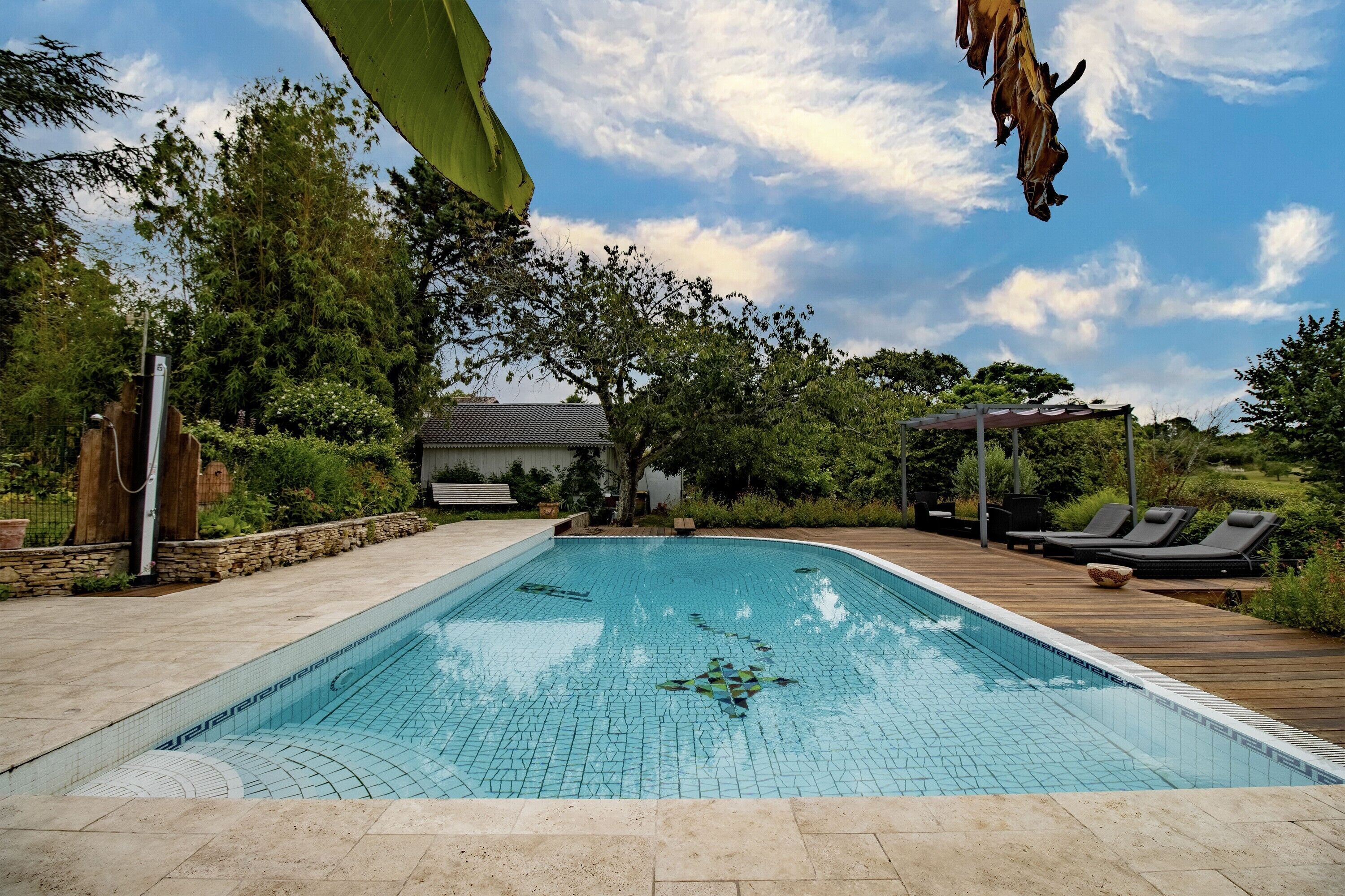Une piscine dont les bords sont recouverts de carreaux, entourée d’une terrasse en bois et de chaises longues.