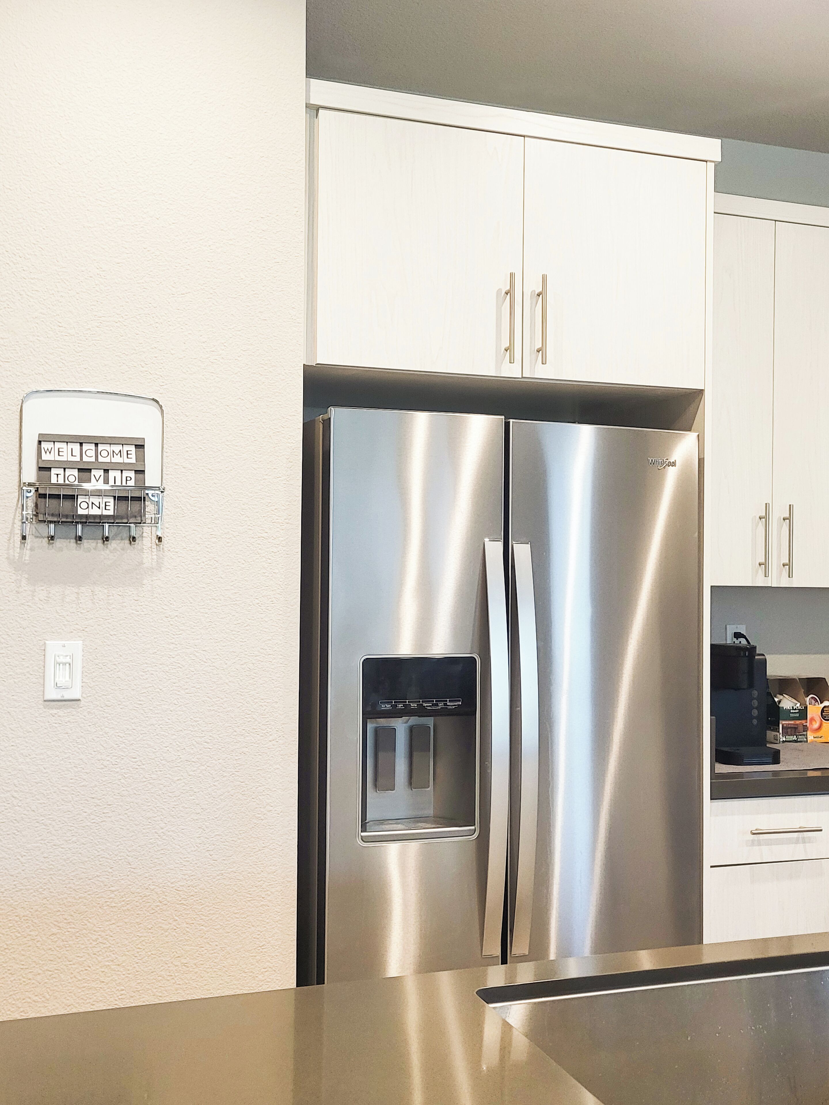 A stainless steel refrigerator with a water dispenser, white cabinets, and a built-in coffee maker.