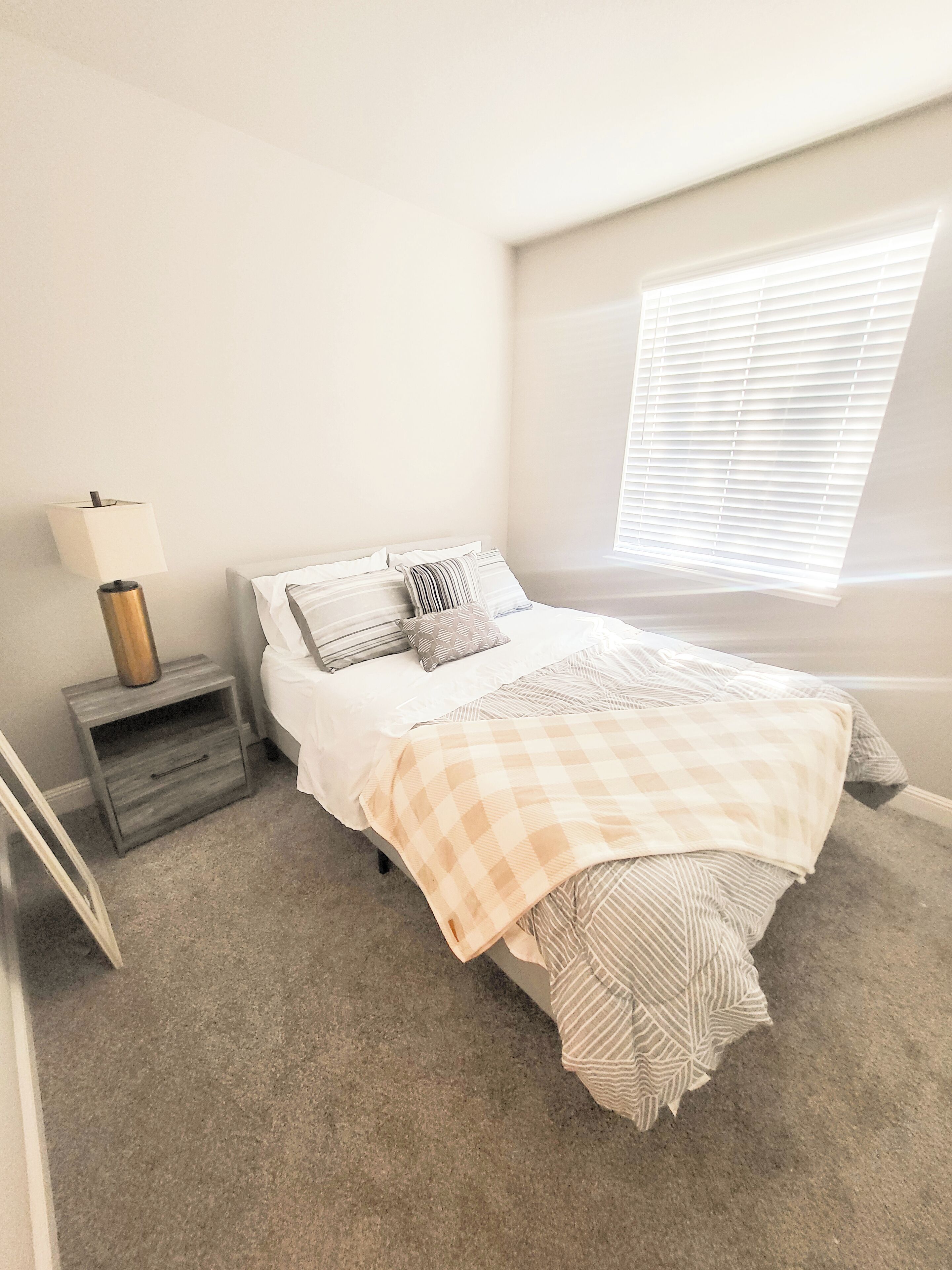 A bedroom with a bed, a nightstand, a lamp, and a window with blinds.