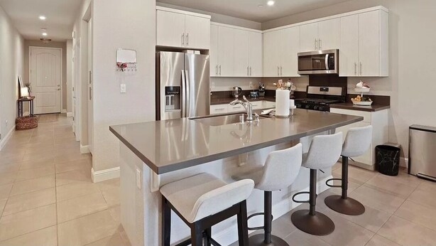 A modern kitchen with white cabinets, a stainless steel refrigerator, a microwave, and a large island with bar stools. - VIP Class One ~ Real Comfort ~ 3 Bedrooms (Lodi)