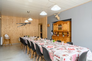 Un coin repas avec une longue table dressée pour un repas, des murs lambrés, une tête de cerf accrochée au mur et un buffet en bois contenant de la verrerie.