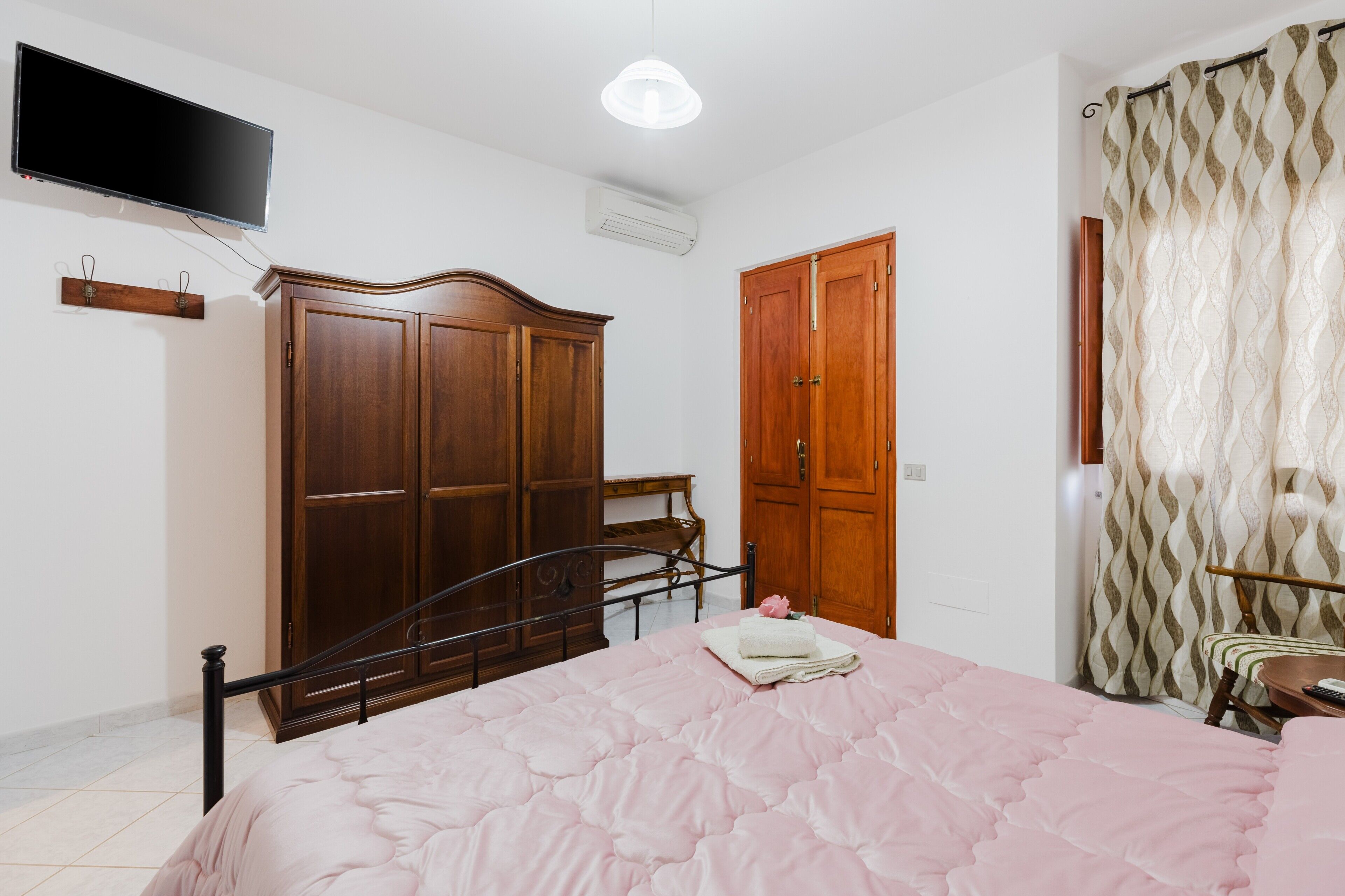 A bedroom with a bed, wardrobe, TV, and curtains.