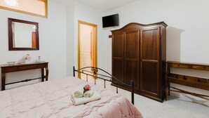 Een slaapkamer met een bed, een houten garderobe, een televisie, een spiegel en een bureau.