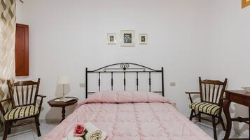 A bedroom with a bed, two chairs, a small table, and three framed pictures on the wall.
