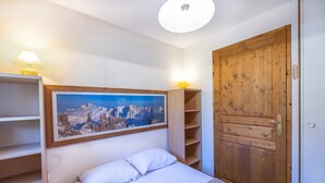 A bedroom with a bed, a wooden door, a shelf with a lamp, and a framed picture on the wall. - Apartment 'Le Jardin Des Neiges' with Balcony (Praz-sur-Arly)