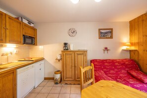 A compact kitchen with wooden cabinets, a microwave, a small refrigerator, a sink, and a dining table. - Apartment 'Le Jardin Des Neiges' with Balcony (Praz-sur-Arly)