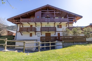 A multi-story building with balconies, a wooden fence, and a grassy area in front.